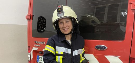 Stine steht vor einem roten Transporter in ihrer Feuerwehruniform